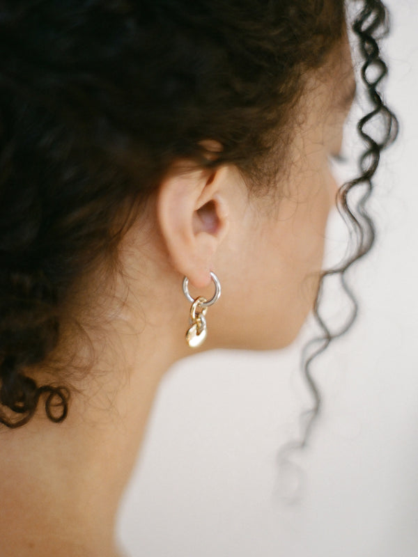 Model wearing a pair of silver hoops with gold rectangular charms on a neutral background.
