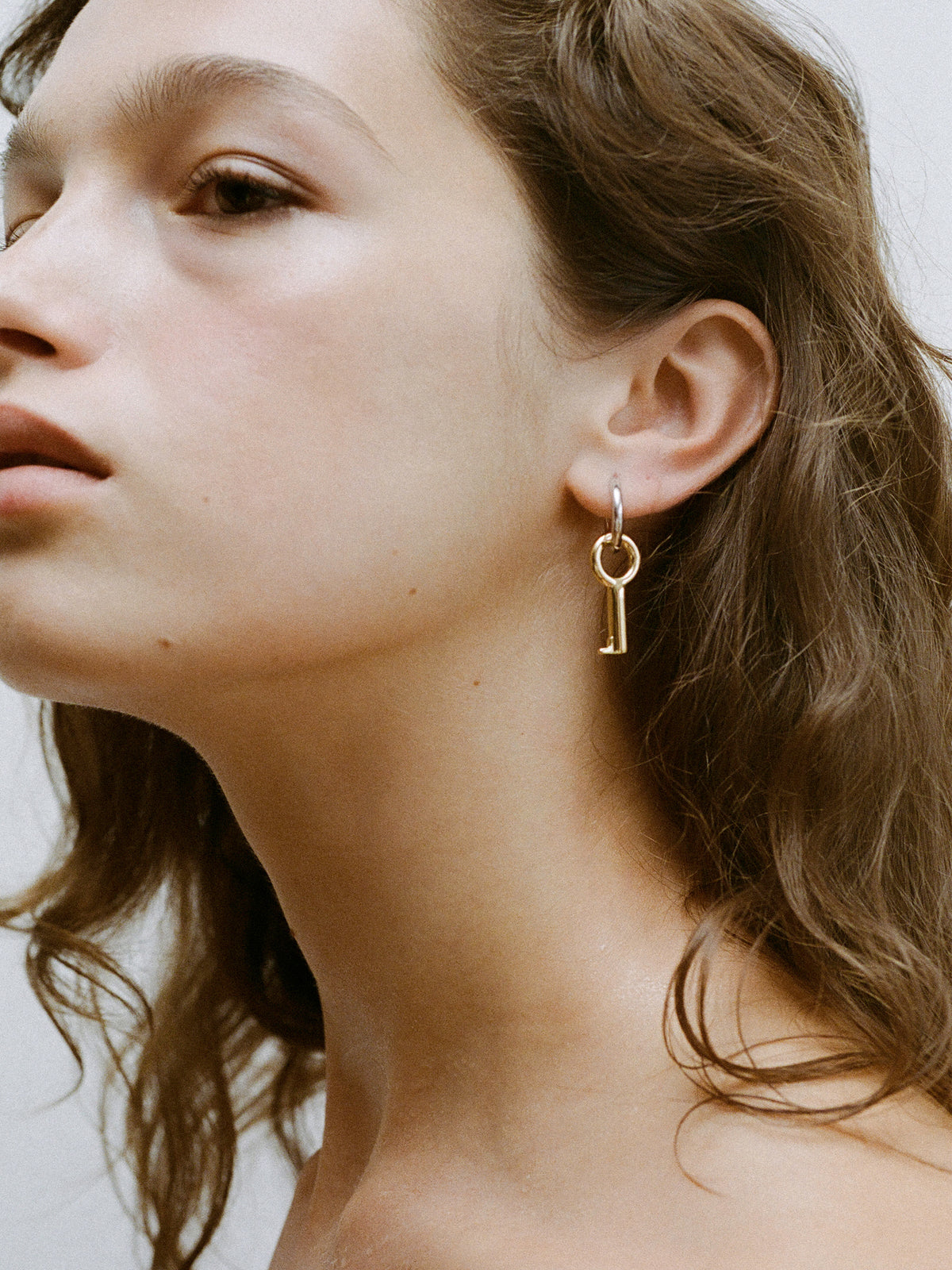 Close-up of model wearing the Two Tone Entra Earring, a petite silver hoop with gold charm detail.