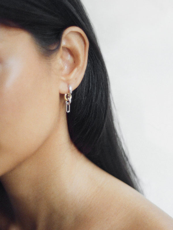 Side profile of model wearing the Two Tone Frena Earring, silver hoop earrings with a dangling gold and silver chain link design, shown on a neutral background.