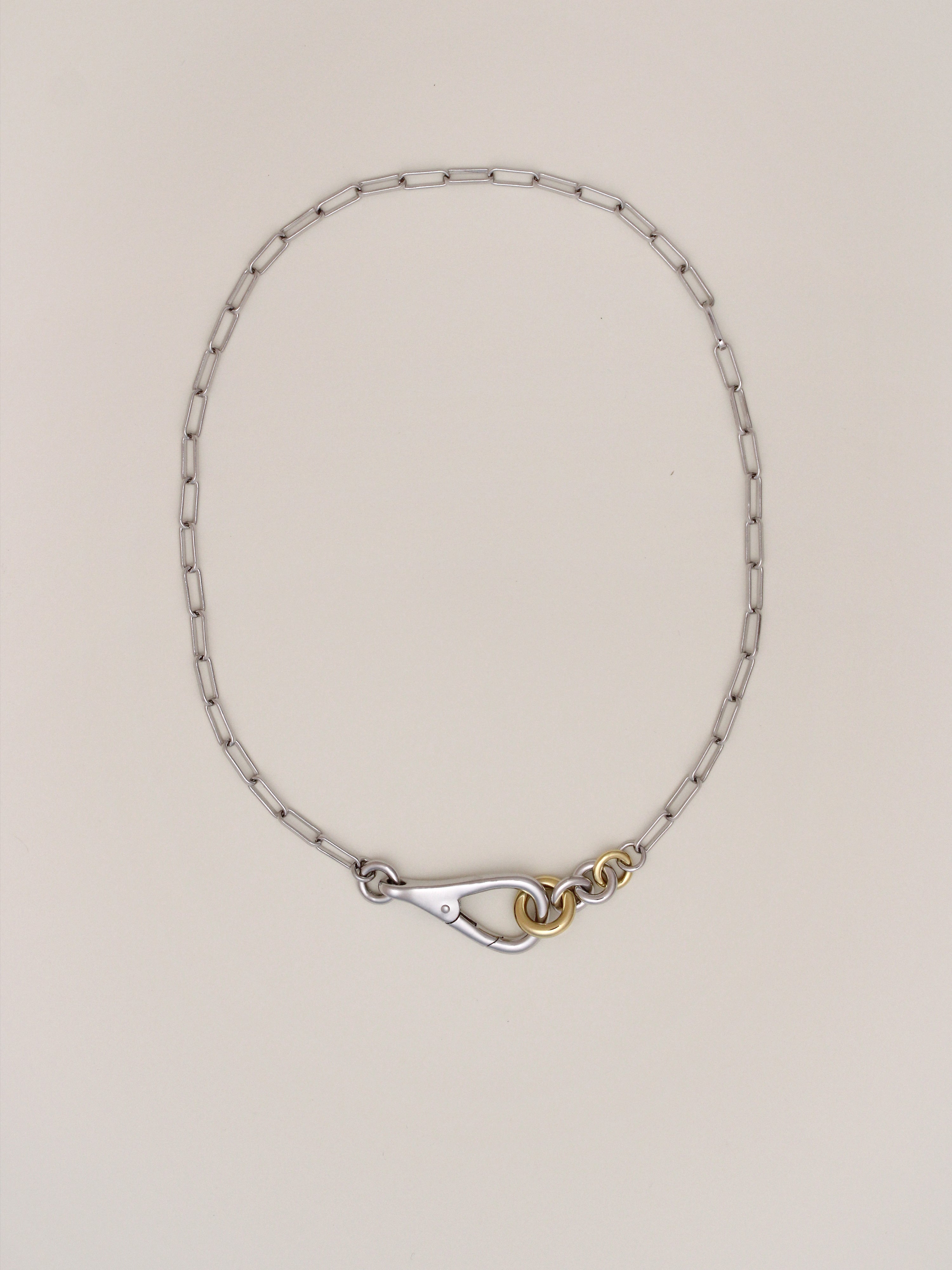 Two Tone Frena Necklace, a silver-toned oval chain necklace with a silver toggle clasp and gold jump ring, displayed on a neutral background.