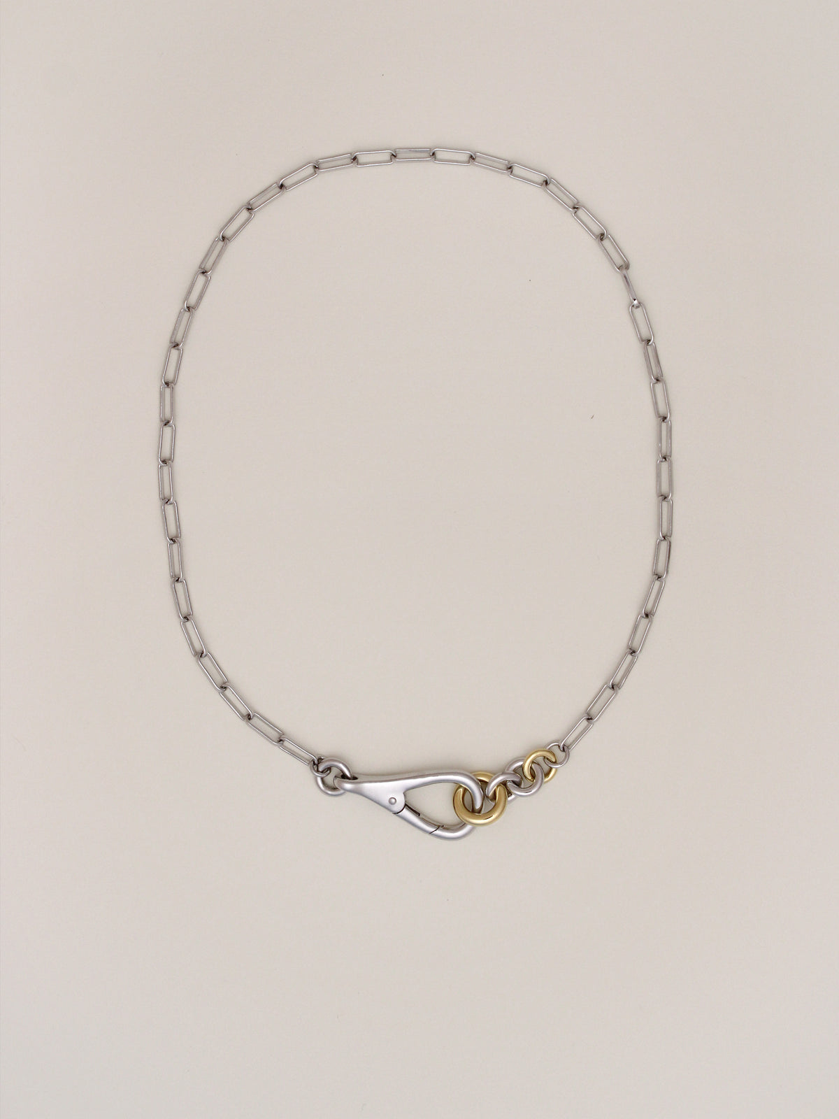 Two Tone Frena Necklace, a silver-toned oval chain necklace with a silver toggle clasp and gold jump ring, displayed on a neutral background.