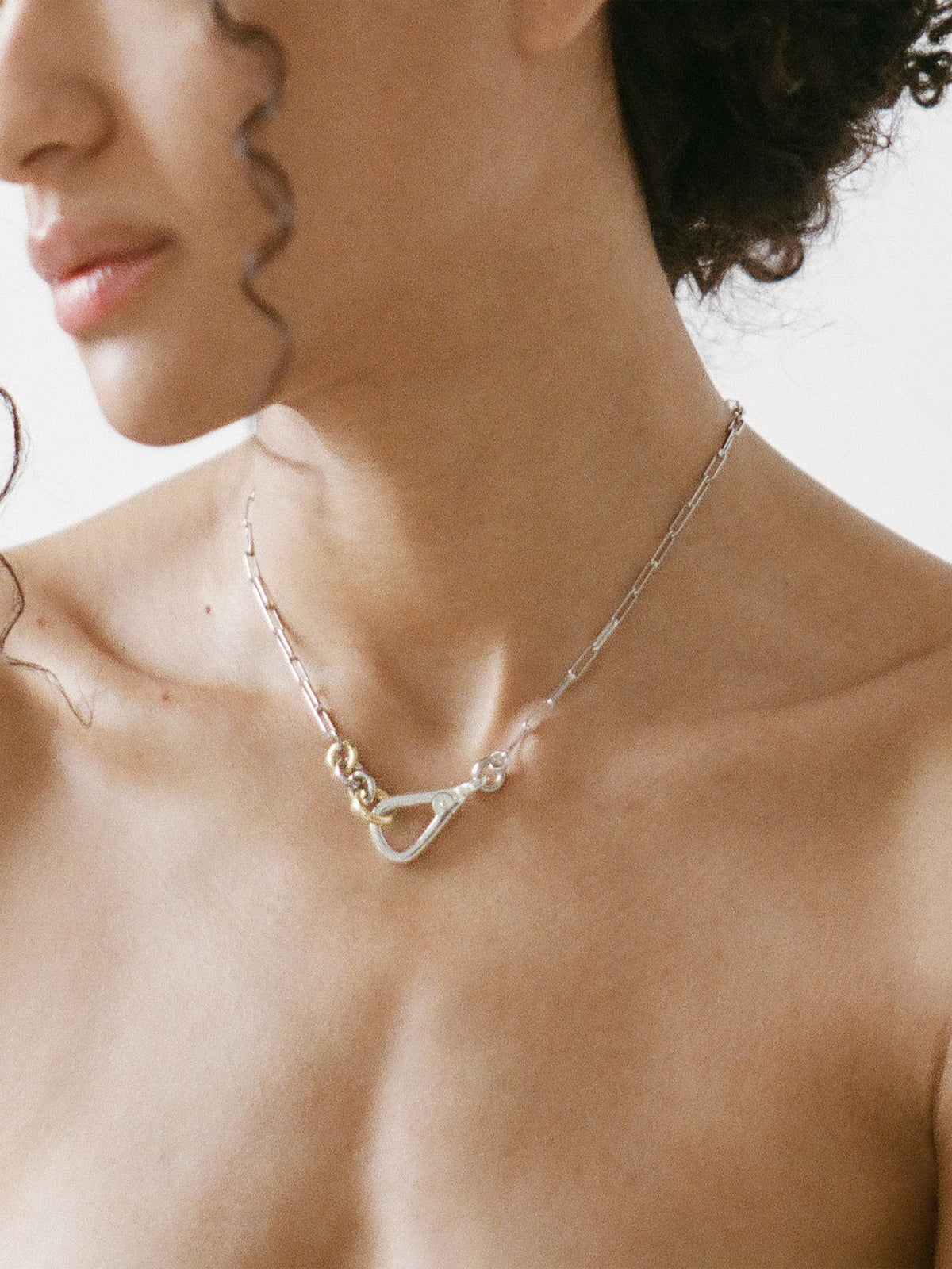 Model wearing the Two Tone Frena Necklace, a silver-toned oval chain necklace with a silver toggle clasp and gold jump ring, displayed on a neutral background.