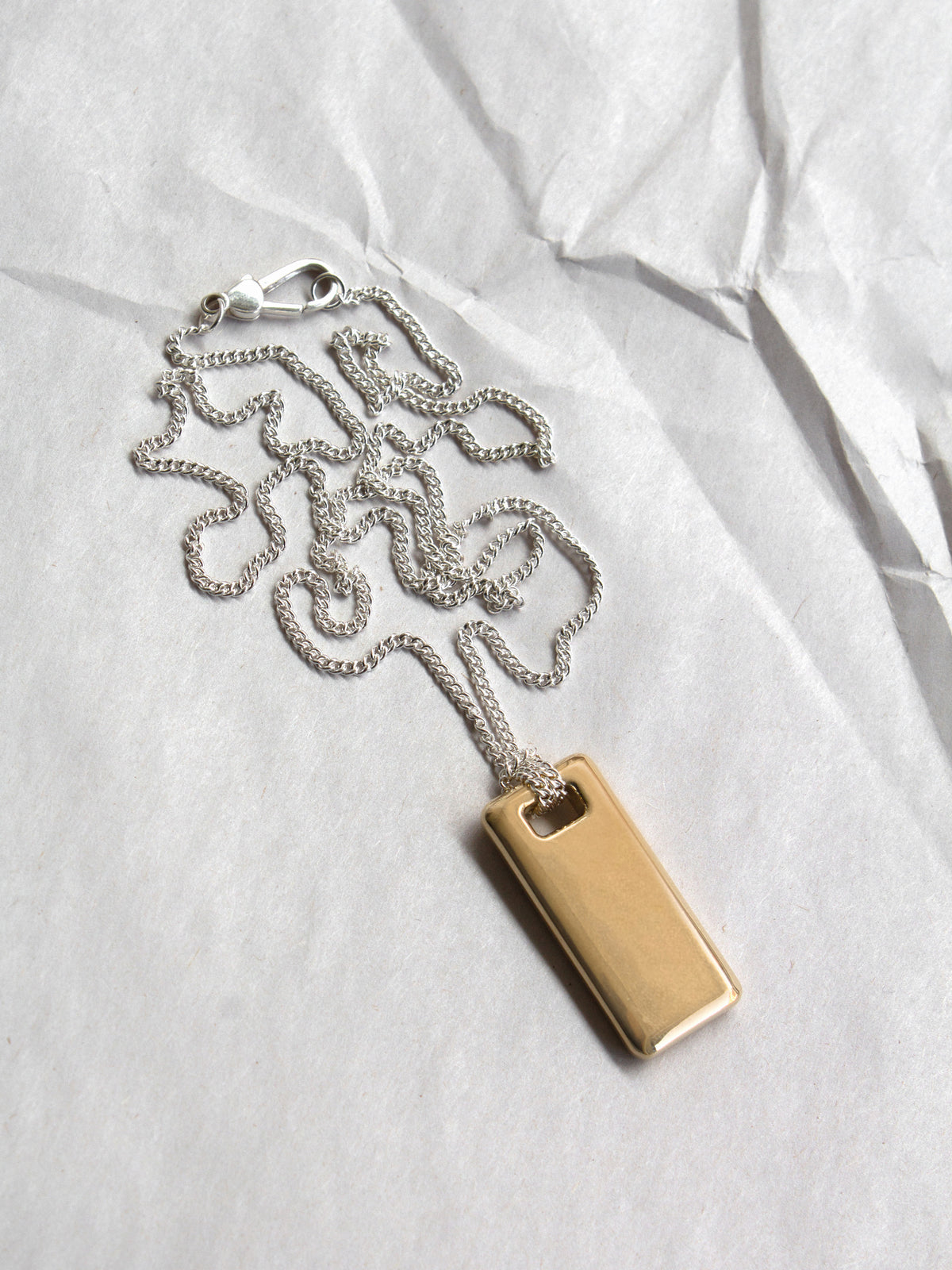 Gold rectangular pendant on a sterling silver chain laid flat on a paper background.
