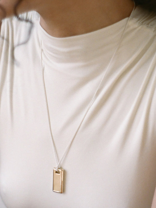 Model wearing a gold rectangular pendant on a sterling silver chain against a neutral background.