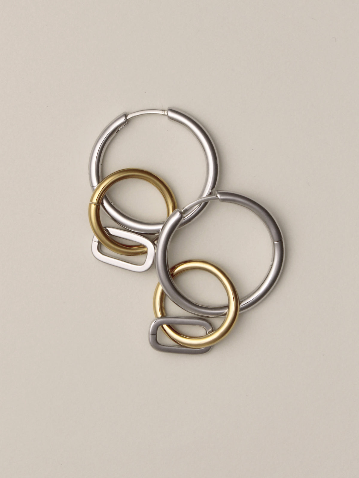 Laura Lombardi Two Tone Passa Earrings, medium silver hoops with a gold circular charm and a silver oval charm, layered on top of eachother.
