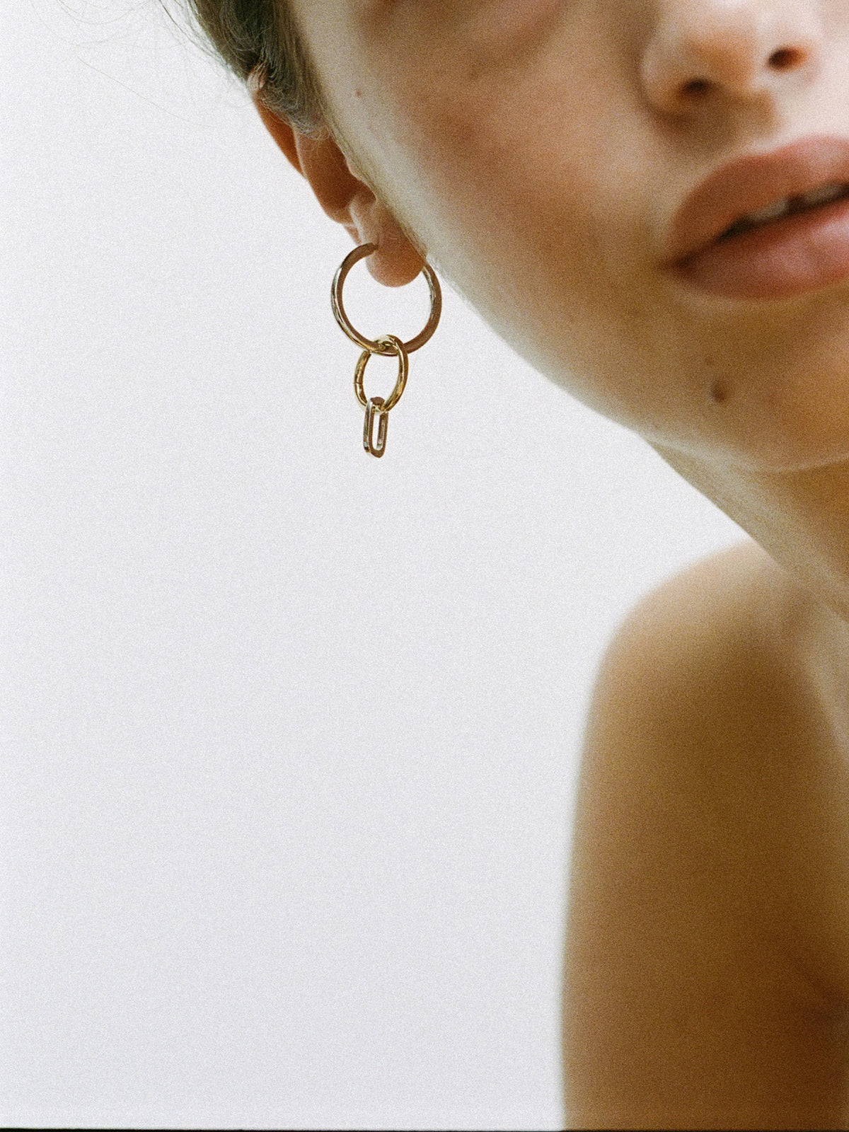 Closeup of model wearing a Laura Lombardi Two Tone Passa Earring, medium silver hoop with a gold circular charm and a silver oval charm.