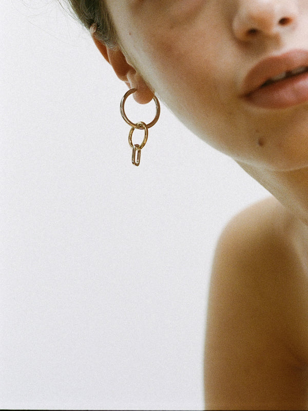 Closeup of model wearing a Laura Lombardi Two Tone Passa Earring, medium silver hoop with a gold circular charm and a silver oval charm.