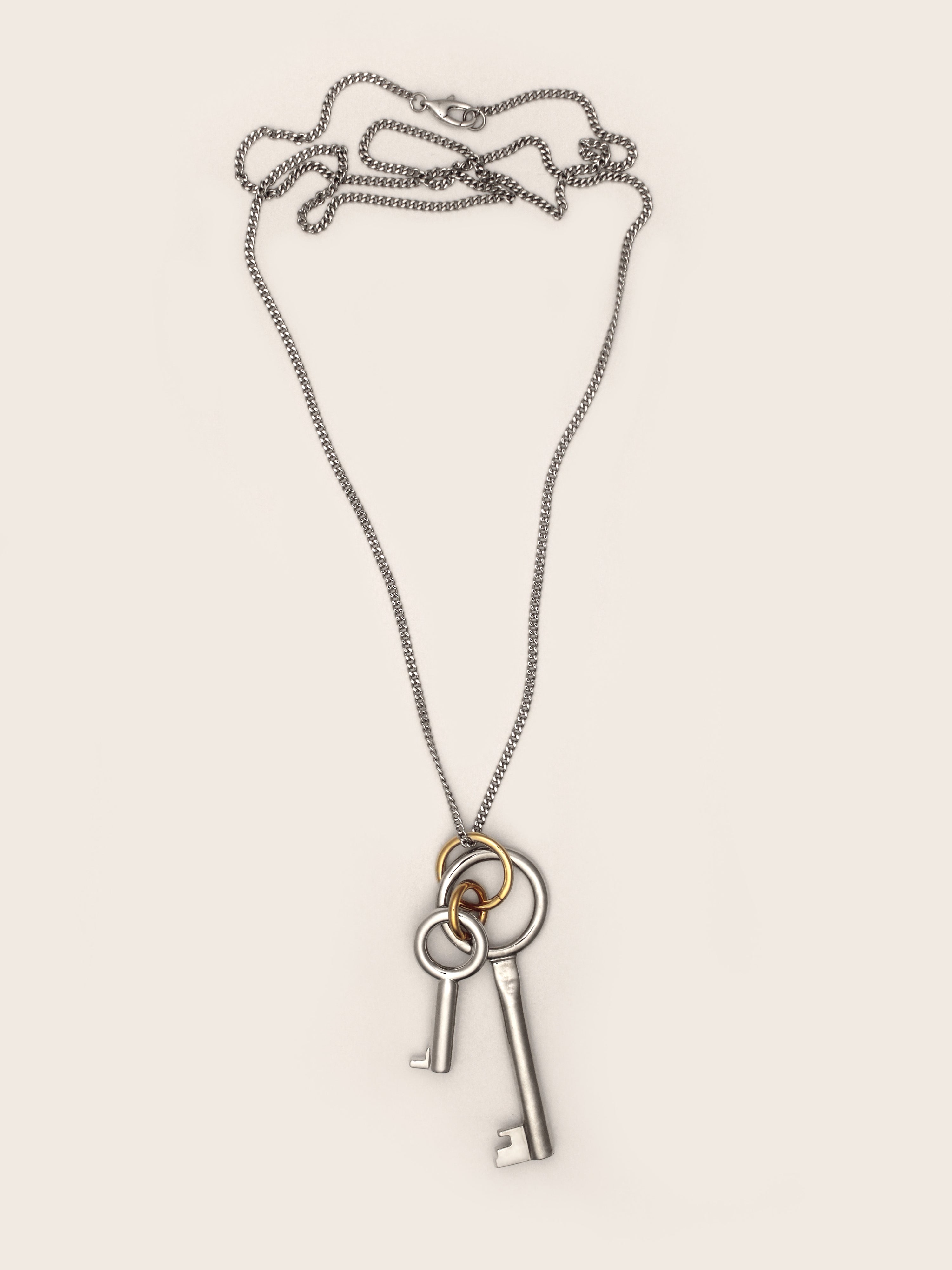Laura Lombardi Permesso Necklace, a silver-toned key pendant necklace with a large and small silver key charm and gold accent ring, shown on a neutral background.