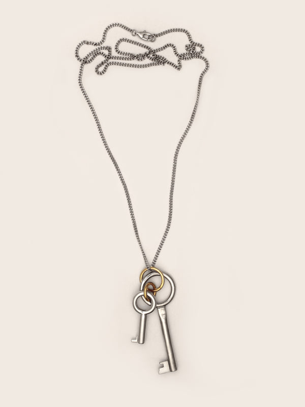 Laura Lombardi Permesso Necklace, a silver-toned key pendant necklace with a large and small silver key charm and gold accent ring, shown on a neutral background.
