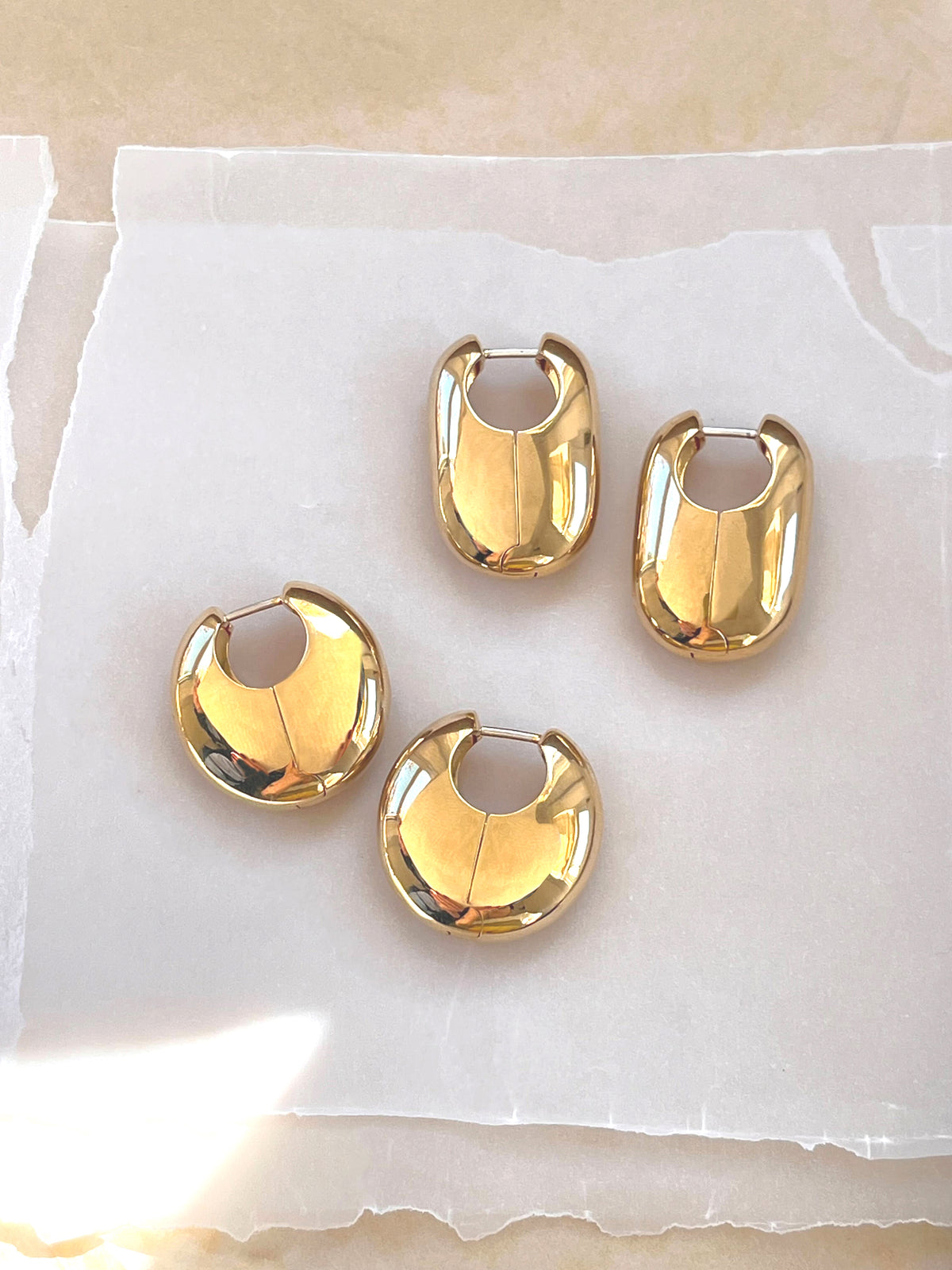 Vola and Ferma Earrings in gold on a neutral background.