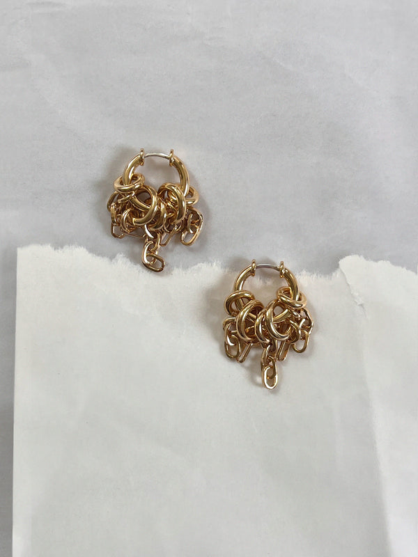 Pair of Laura Lombardi gold Stalla fringe earrings laid flat on a neutral background